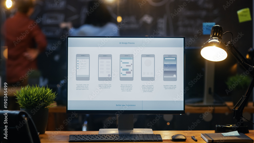 Poster Personal Computer with Mobile Application Design Showing on the Monitor Stands on the Office Desk, In the Background People Work on a Blackboard Wall in the Creative Office.