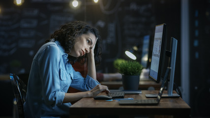 Tired, Overworked Female Financier Holds Her Head in Hands while Working on a Personal Computer. In...