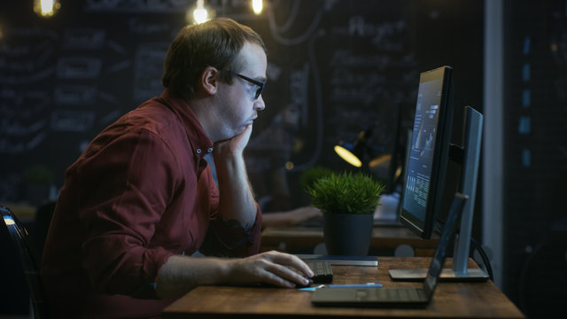 Stressed, Overworked Financier Makes Face Palm Gesture in Frustration while Working on a Personal Computer with Statistics Showing on the Screen. In the Background Creative Office.