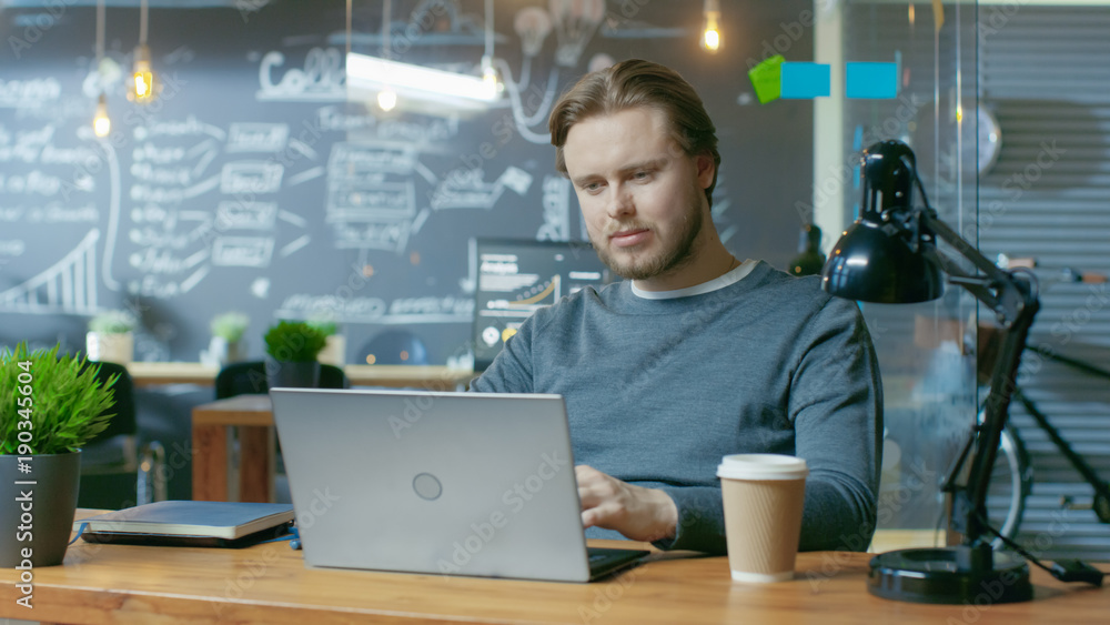 Poster Handsome Young Office Employee Thinks on a Problem Solution While Typing on a Laptop Computer. He's Working in the Creative Stylish Office.