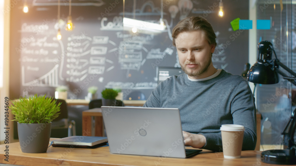 Poster Handsome Young Office Employee Thinks on a Problem Solution While Typing on a Laptop Computer. He's Working in the Creative Stylish Office.