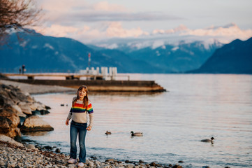 One happy kid girl playing by lake Geneva at sunset with swiss mountains Alps on background. Image taken in Lausanne, Switzerland