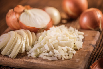 close up of chopped, sliced, halved and whole onion on wood table 