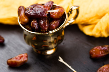 Dry fruit dates in golden cup near slate black heart. Copy space.