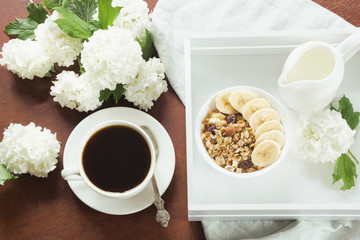 A healthy breakfast with a cup of coffee, muesli,bananas and decor with flowers of viburnum in a country house.