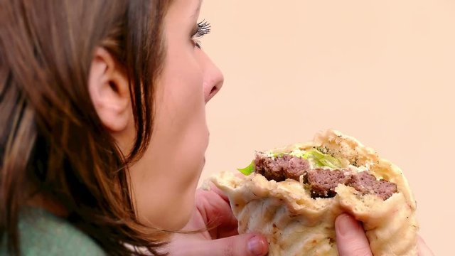Young woman is eating a juicy hamburger with pork and green salad, 4k Video Clip