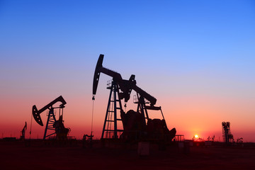 Working oil derrick in field under the setting sun