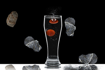 Glass with water and falling stones on a black background