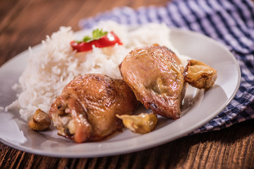 chicken tights upper leg on white plate with rice on wood table. 