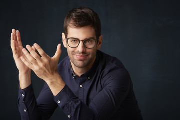 Fototapeta premium He's completely puzzled. Portrait of smiling young man with his arms raised and wondering at dark background. 