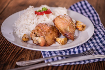 chicken tights upper leg on white plate with rice on wood table. 
