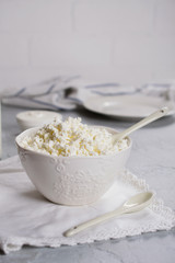 Cottage cheese from fresh milk in a white bowl. On gray concrete background.