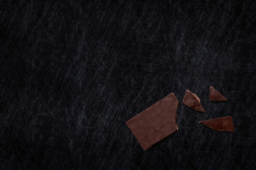 Broken dark chocolate bar isolated on a scratched slate chopping board. Horizontal composition. Top...