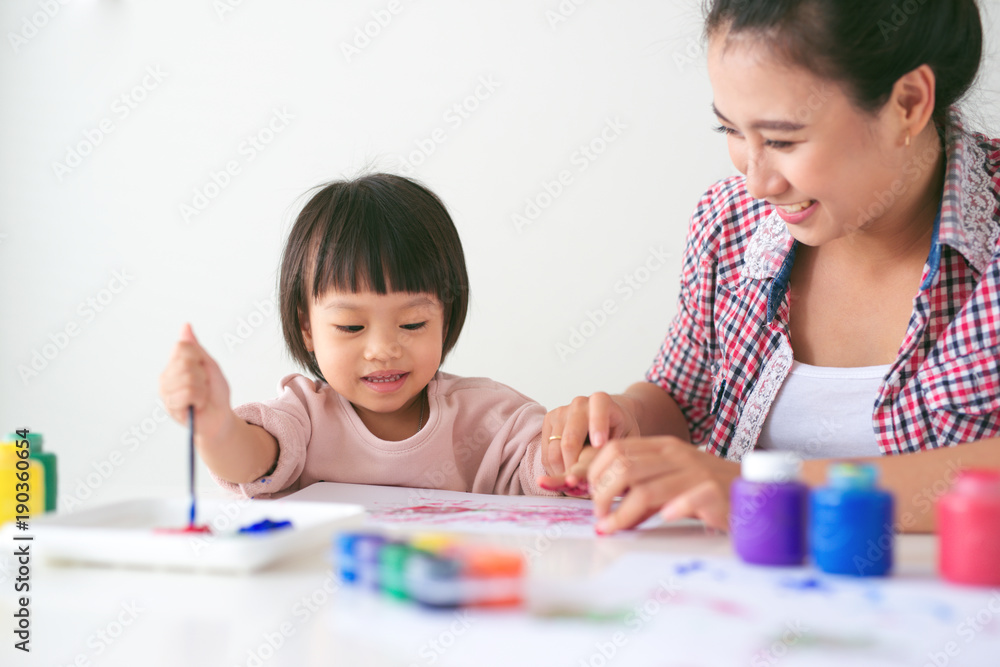 Wall mural Little asian girl painting with paintbrush and colorful paints