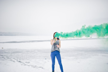 Young girl with green colored smoke bomb in hand in winter day.