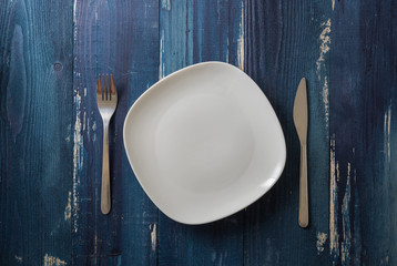 White Plate on blue wooden background with utensils
