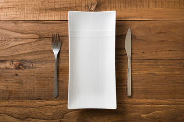 White rectangular Plate with fork and knife on brown wooden background