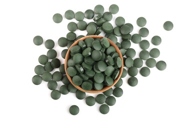 heap of Spirulina tablets algae nutritional supplement in wooden bowl isolated on white background close up top view