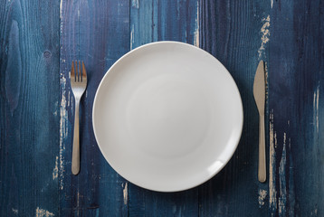 White Plate on blue wooden background with utensils