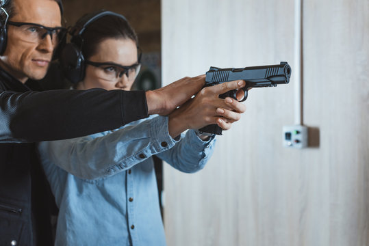 male instructor helping customer to shoot with gun in shooting range