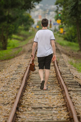 Young man on train tracks with his Ukulele walking