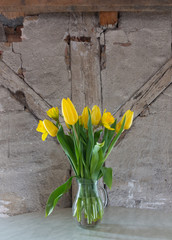 Yellow tulips and daffodils in front of the wall of an attic.