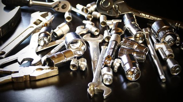 The tool is made of steel on the table in the workshop. The master selects the instrument with his hand. A beautiful chrome set of tools.