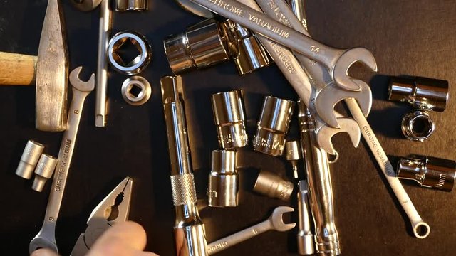 The tool is made of steel on the table in the workshop. The master selects the instrument with his hand. A beautiful chrome set of tools.