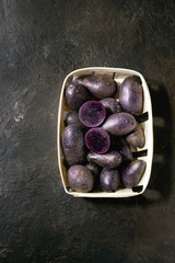 Raw purple uncooked organic potatoes named prunelle, whole and slice, in market baskets over dark...