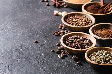 Variety of grounded, instant coffee, different coffee beans, brown sugar, spices in wooden bowls over dark texture background. Copy space