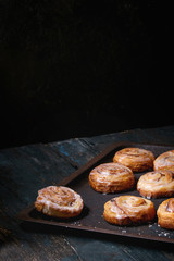 Homemade glazed puff pastry cinnamon rolls with custard and raisins on oven tray over old dark blue wooden background. Rustic style
