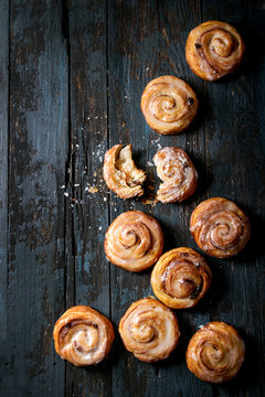Homemade glazed puff pastry cinnamon rolls with custard and raisins over old dark blue wooden background. Top view, space. Rustic style