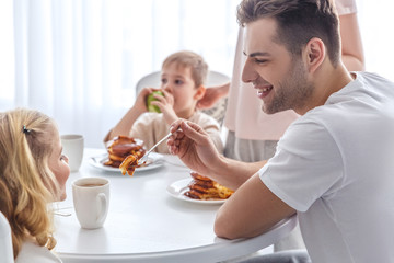 Obraz na płótnie Canvas father feeding his daughter with pancake on family breakfast