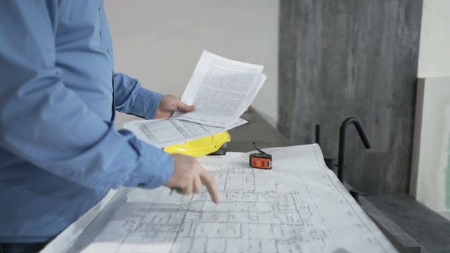 Man reading, comparing documents and blueprints by table at new home
