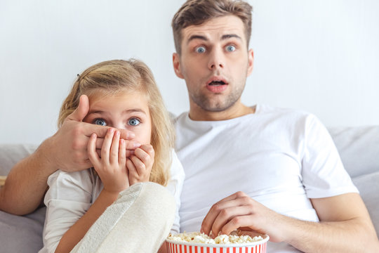 scared father and daughter watching horror movie at home