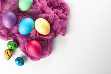 Scattered painted easter chicken and quail eggs on a white background with fuchsia gauze napkins