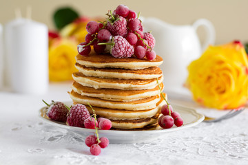 Stack of pancakes with raspberry, red currant, cream and honey on white table cloth