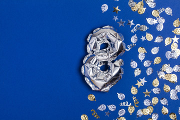 Silver foil number 8 balloon on a blue background with glitter gonfetti