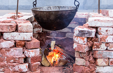 hanging big black sooty cauldron over  bonfire surrounded by a brick wall, camping vacation outdoor kitchen