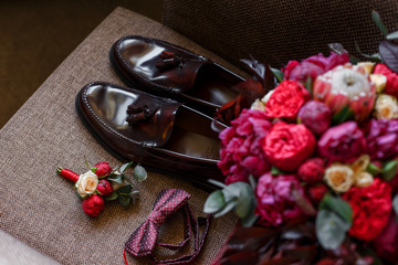 Set of trendy mens clothes and accessories in red colors. Groom red dotted bow tie, lacquered brown shoes, wedding trendy bouquet and boutonniere on the chair