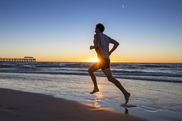 silhouette young dynamic athlete runner man with fit strong body training on Summer sunset beach...