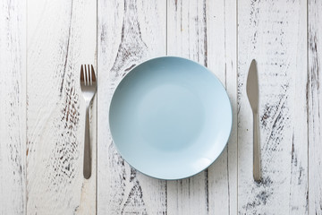 Blue Plate on white wooden background with utensils
