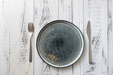 Plate on white wooden background with utensils