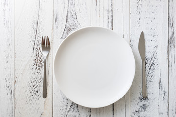 Plate on white wooden background with utensils