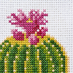 Embroidered cactus cross on white canvas in a frame on a light background is isolated close-up,...