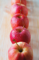 middle angle view of organic pink lady apples arranged in a row. Apples with water drops on light wooden background.