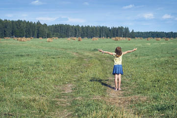 Schoolgirl standing on the countryside field with raised hands