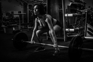Fototapeta na wymiar Portrait of a beautiful girl who crouches with a barbell in the gym. Sport life. bw