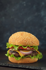 Homemade burger with beef, cheese, tomato, onion, salad on stone board.