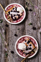 Homemade cherry sponge cake served with ice cream on vintage plates on old wooden table. Selective focus 